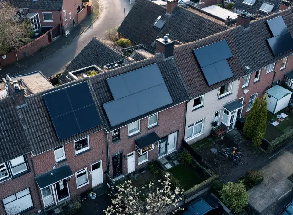 Een rij rijtjeshuizen van bovenaf gezien, sommige daken met zwarte zonnepanelen en andere zonder